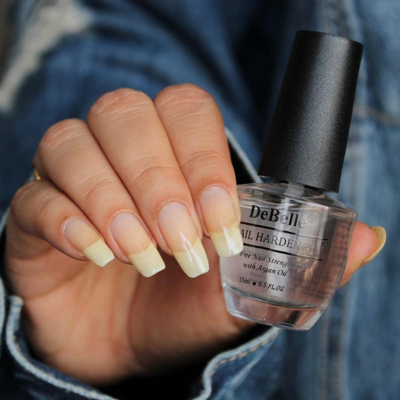 Holding a DeBelle Nail hardner - Close-up view of the nail Hardner and Nails with the bottle against a blue jeans background.