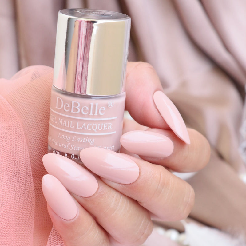 Holding a DeBelle Peony Blossom nail lacquer with the pink background and a manicured Nails