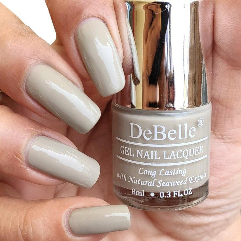 holding a debelle grey nail polish bottle with a painted nails and a white background.