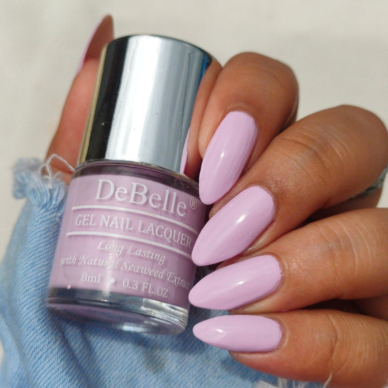 Holding Lavender Nail polish Bottle from Debelle with the painted nail of same shade against a cream background.
