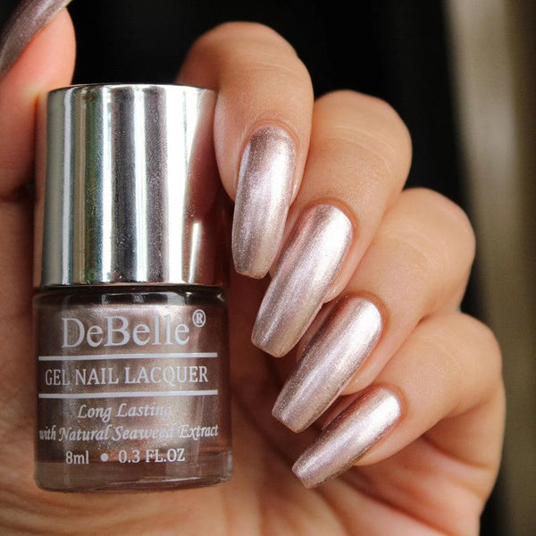 holding a Debelle blush rose gold nail polish with the manicured nails and a dark background.