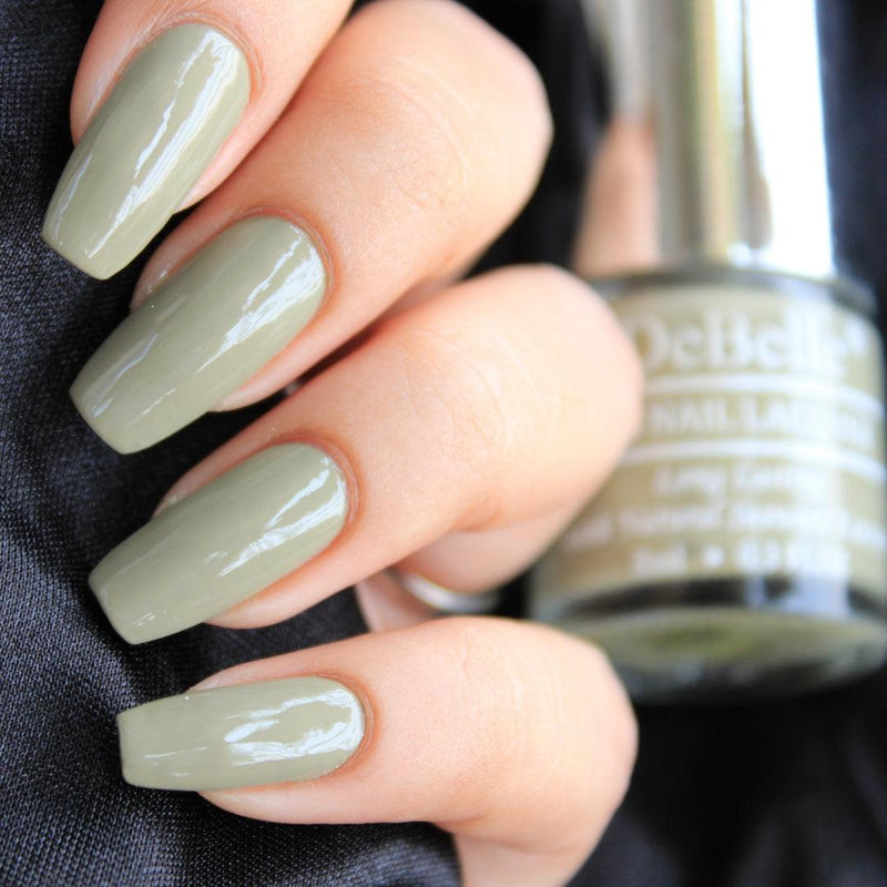 close-in view of beautifully manicured nails with debelle olive green nail polish against a blurry background.