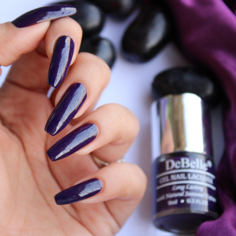 Close-in view of painted nails with Debelle Dark Violet Nail polish against a white with purple background.