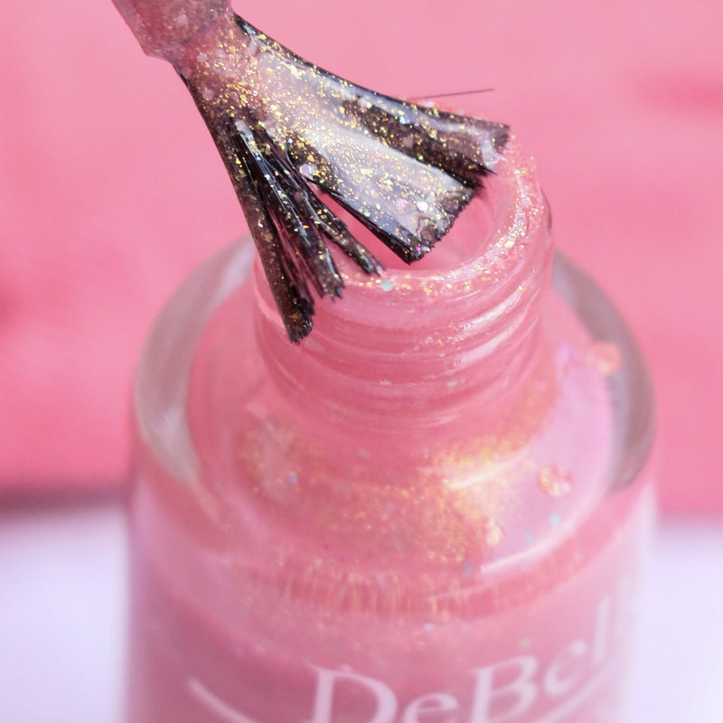 Debelle pink mauve nail polish with opened bottle against a pink background with a nail brush