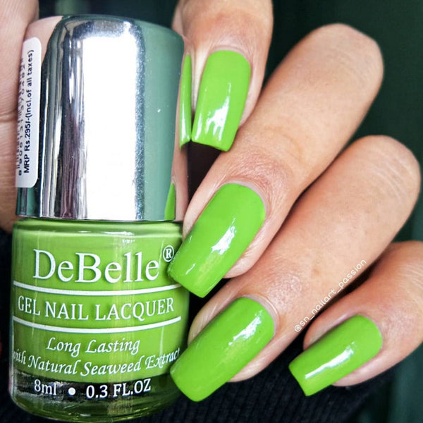 DeBelle parrot green -close-up view of nail polish bottle with the manicured nail with the elegance against dark background.