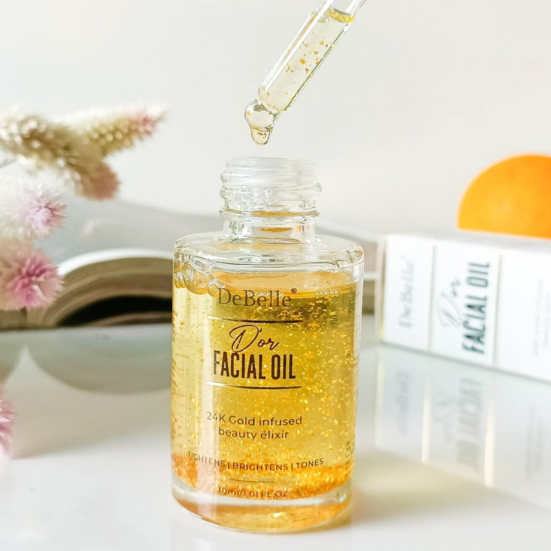 opened bottle of luxurious Debelle Facial Gold oil with the droplet from the cap against a white surface with a book