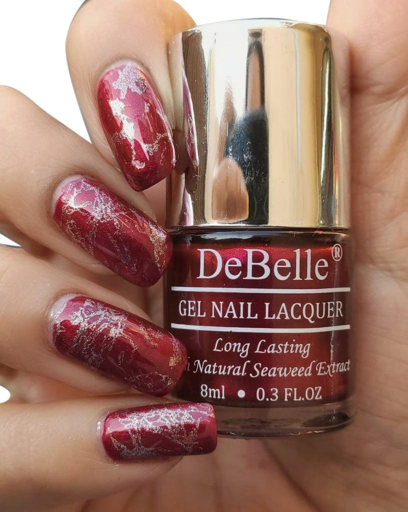 DeBelle Deep Maroon pearl finish Nail Polish Close-up view of the nail polish bottle and manicured nails has white background 