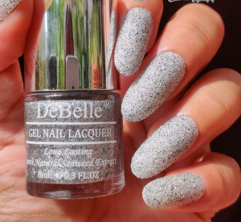 DeBelle Silver with Black Glitter Nail Polish - Close-up view of the nail polish bottle and painted nails with added glitter has green background