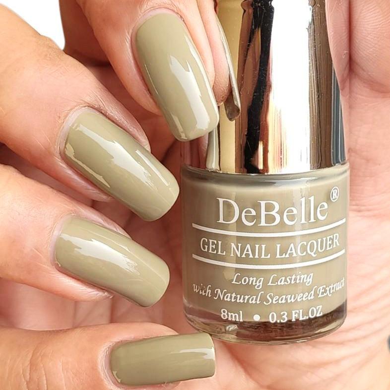DeBelle olive green-close-up view of nail polish bottle with the manicured nail with the elegance against a light background.