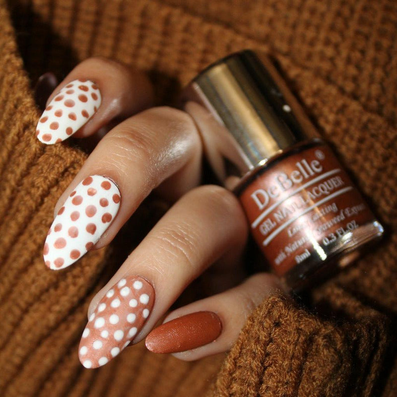 Beautiful nail art with debelle metallic gold nail polish bottle with a beautifully manicured nails against a brown background. 