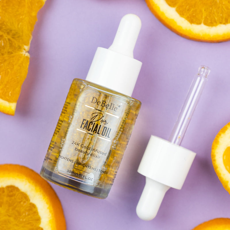 Bottle of Debelle facial Gold oil placed against a pink background with oranges around it.