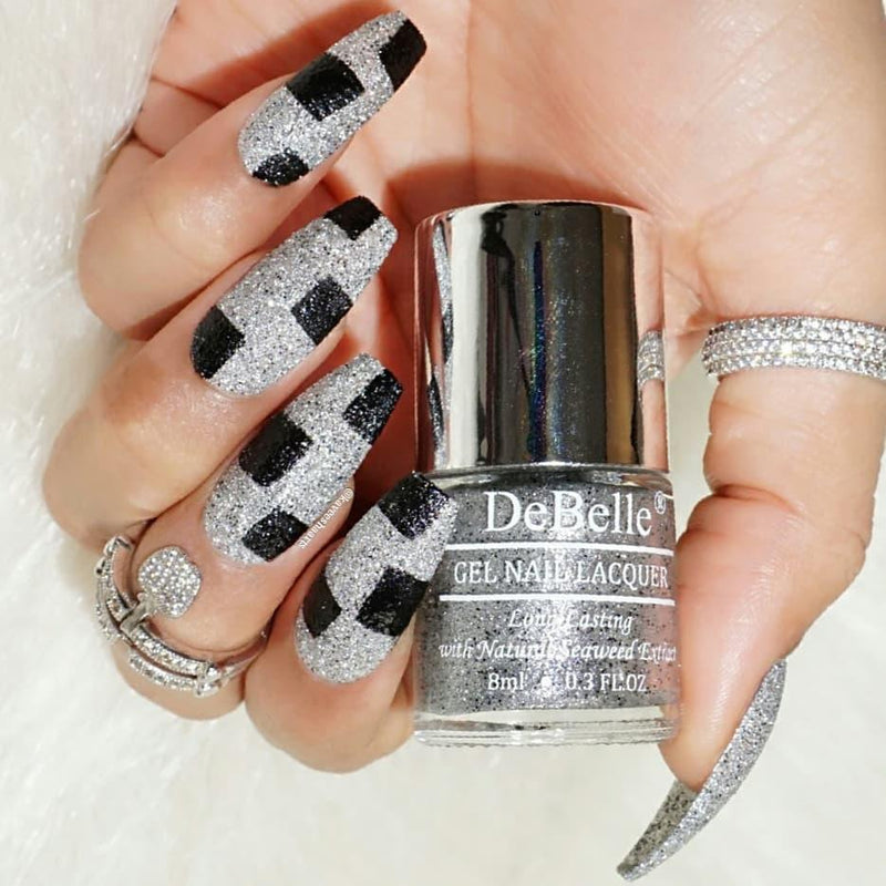 DeBelle Silver with Black Glitter Nail Polish - Close-up view of the nail polish bottle and painted nails with added glitter has white background
