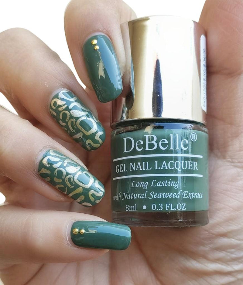 DeBelle olive green-close-up view of nail polish bottle with the manicured nail against a dark background.