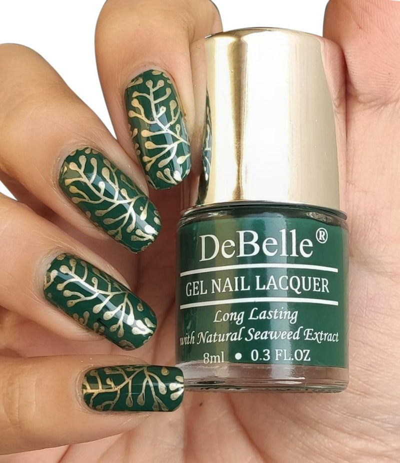 DeBelle dark green -close-up view of nail polish bottle with the manicured nail with the elegance against a white background.