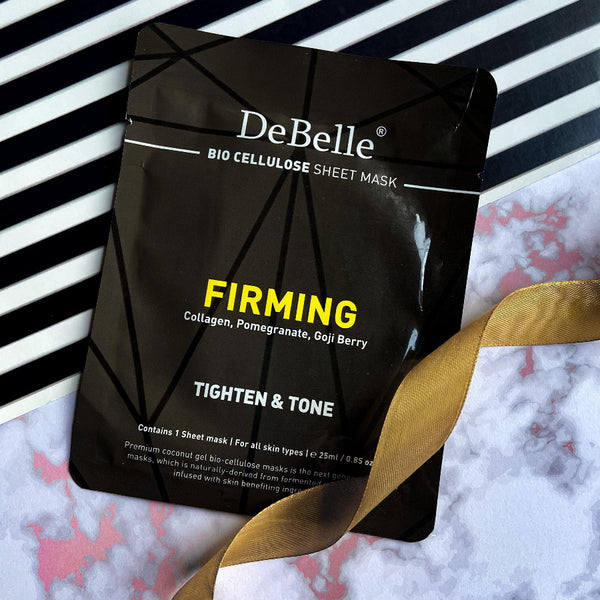 DeBelle Bio Cellulose Face Sheet Mask Firming against a blaxk and white stripes with a golden ribbon.
