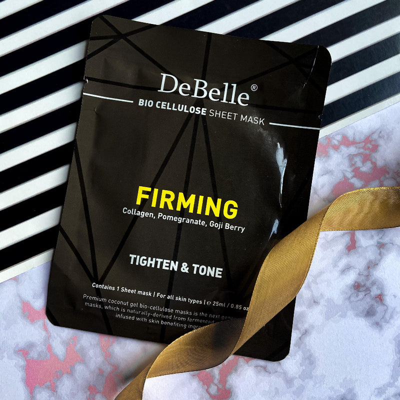 DeBelle Bio Cellulose Face Sheet Mask Firming against a blaxk and white stripes with a golden ribbon.