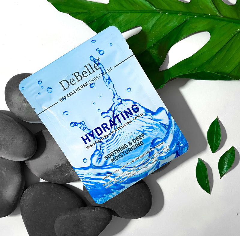 Close-up view of Debelle Hydrating sheet mask with a green leaf and a white surface with blacks stones