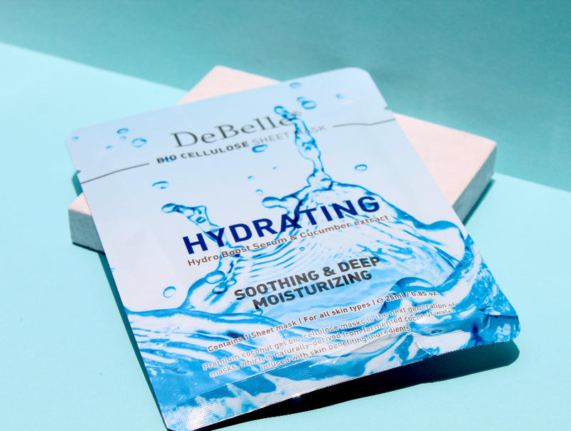 Close-view of Debelle Hydrating sheet mask with a green leaf and a blue surface.