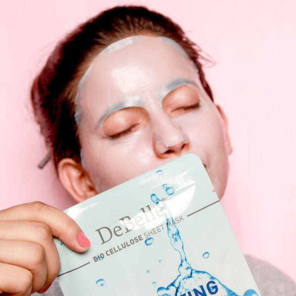 women wearing a Debelle hydrating sheet-masks feeling relaxed against a pink surface.