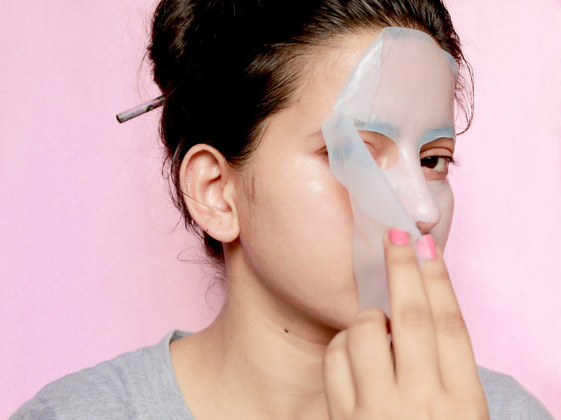 women removing DeBelle hydrating sheet mask after using it against a pink background