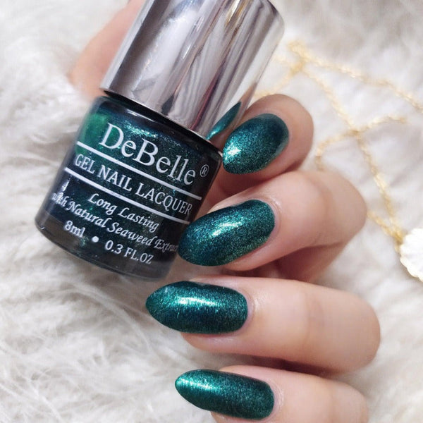 Holding DeBelle Emarald Green nail polish with a beautifully manicured nails against a white surface background.