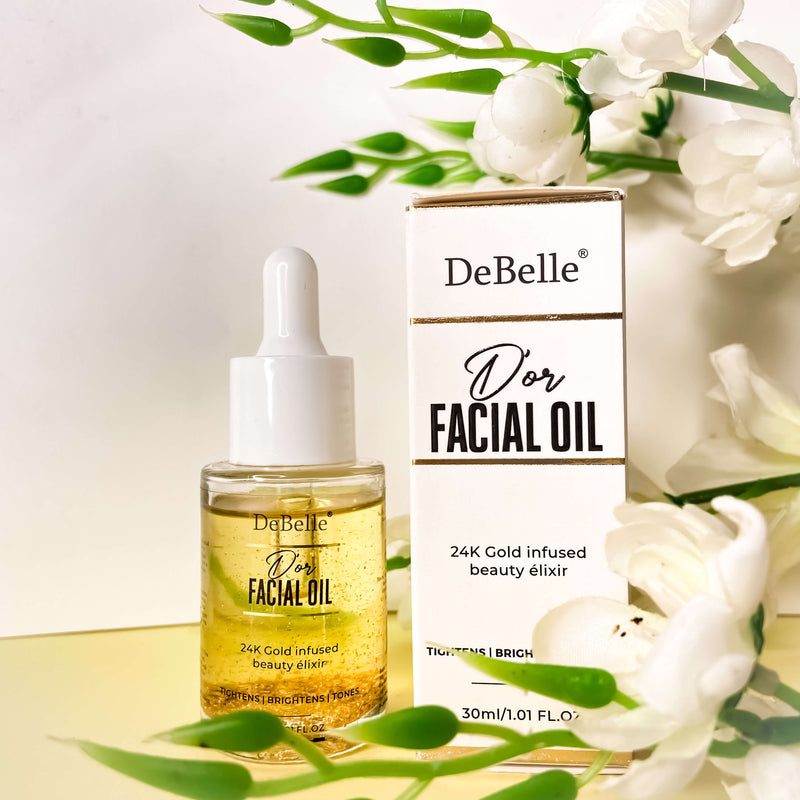 Debelle Facial Gold Oil: Luxurious bottle of gold-infused facial oil surrounded by flowers on a pristine white background.