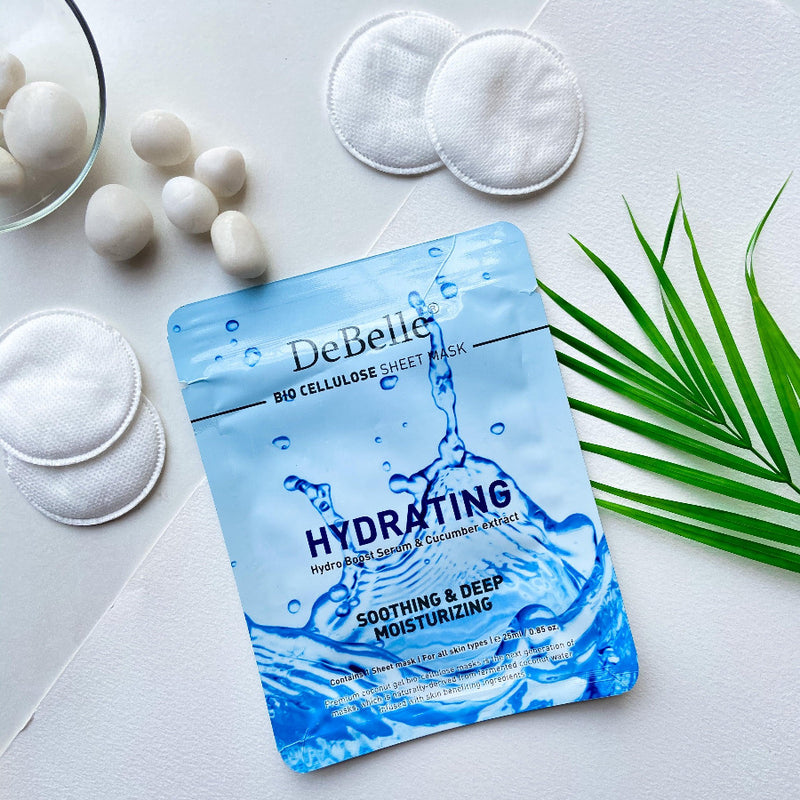 Close-view of Debelle Hydrating sheet mask with a green leaf and a white surface with white stones and a green leaves .