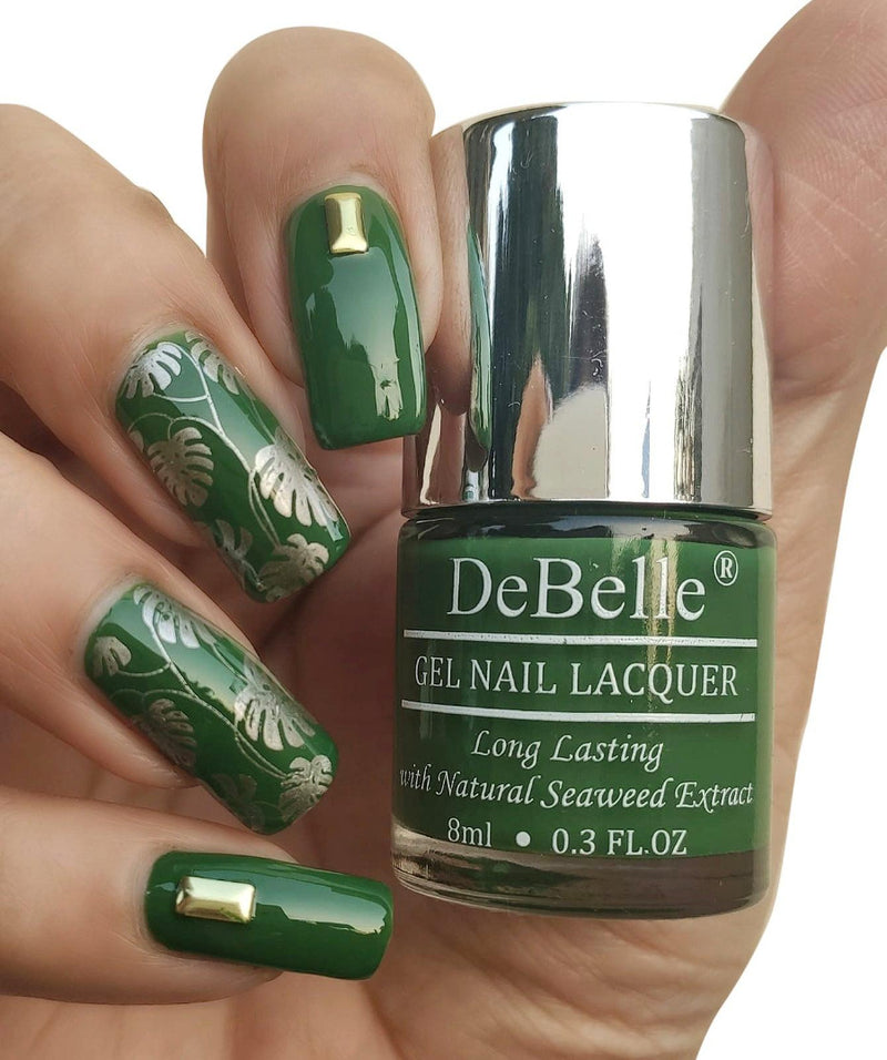 DeBelle dark jade green -close-up view of nail polish bottle with the manicured nail with the elegance against white background and a nail art.