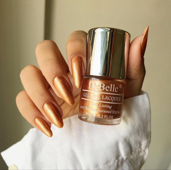 debelle Rustique gold nail polish bottle with a beautifully manicured nails against a white creamy backrgrond.