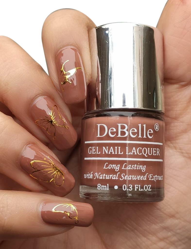 Holding a DeBelle nail lacquer bottle with a manicured nail and a nail art against a white background.