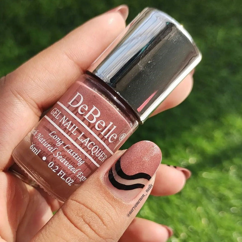 Holding a Mauve with Micro Shimmer Nail polish Bottle from Debelle with the painted nail of same shade has green background