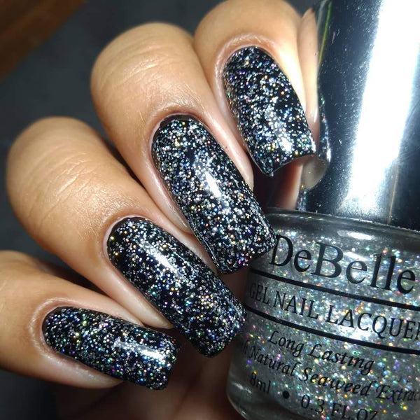 DeBelle Nail Shimmer Top Coat- Close-up view of the nail polish bottle and painted nails has dark background