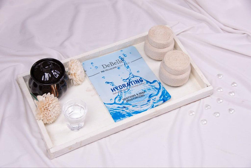 DeBelle hydrating sheet masks placed on a surface table with black pot and white flower.