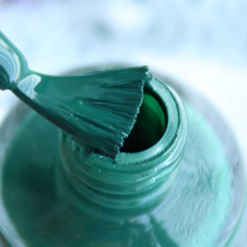 opened bottle of Debelle dark green nail polish with a nail brush with a blurry background.