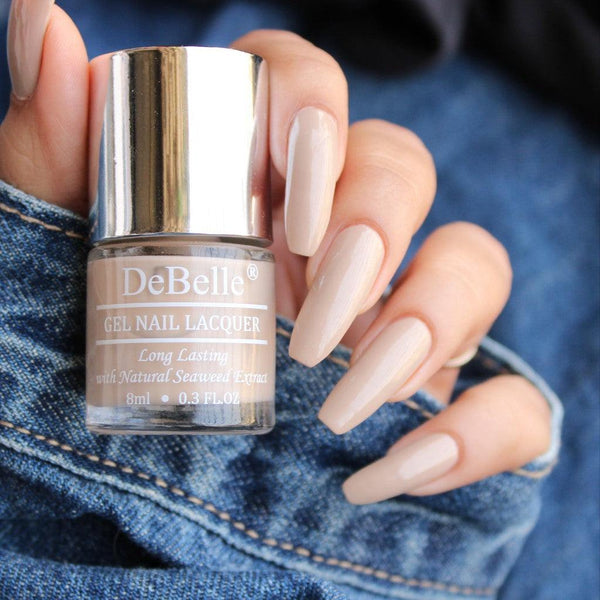 close-in View of DeBelle Victorian Beige holding it with the manicured nails and a dark jeans background 