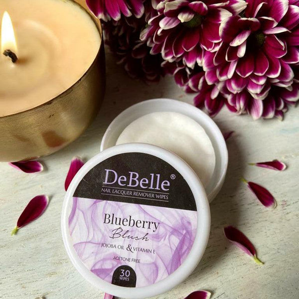 DeBelle Blueberry Blush Nail Lacquer Remover Wipes-close-up view placed with maroon flowers and a white background and a candle.