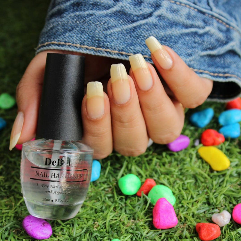 Holding a DeBelle Nail hardner - Close-up view of the nail Hardner and Nails with the bottle against a green background with the colored stones.