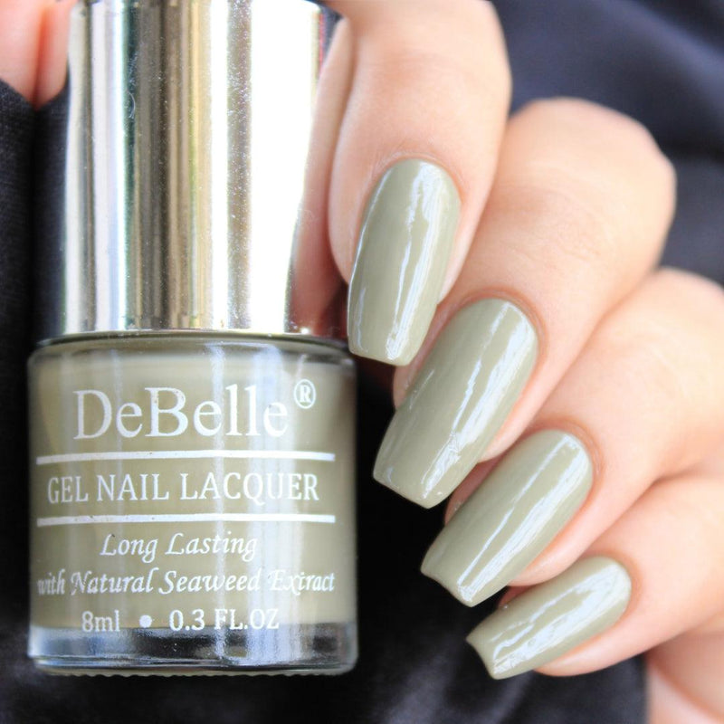 DeBelle olive green-close-up view of nail polish bottle with the manicured nail with the elegance against a dark background.