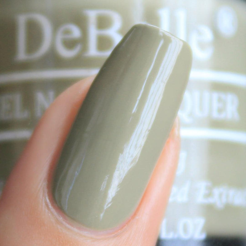 Close-inn view of a nail painted with DeBelle olive green nail polish aginast a  olive green background.