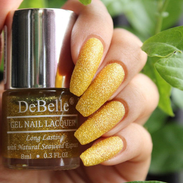 Gleaming lime yellow nails with a touch of glamorous gold glitter, courtesy of DeBelle and a beautifully manicured nail with a green background. 