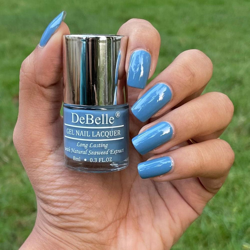 holding a debelle persian blue nail polish bottle against a green background with a manicured nails. 