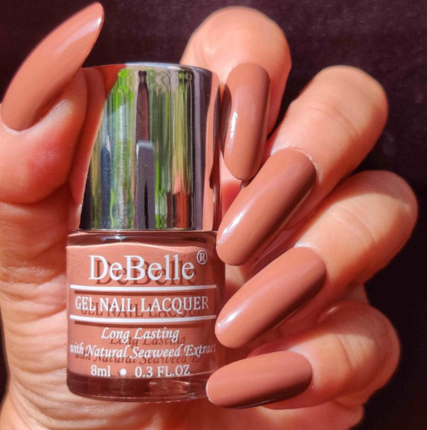 Close-in view of the DeBelle Toffee Rose Nail Lacquer with the beautifully manicured nails and a maroon background. 